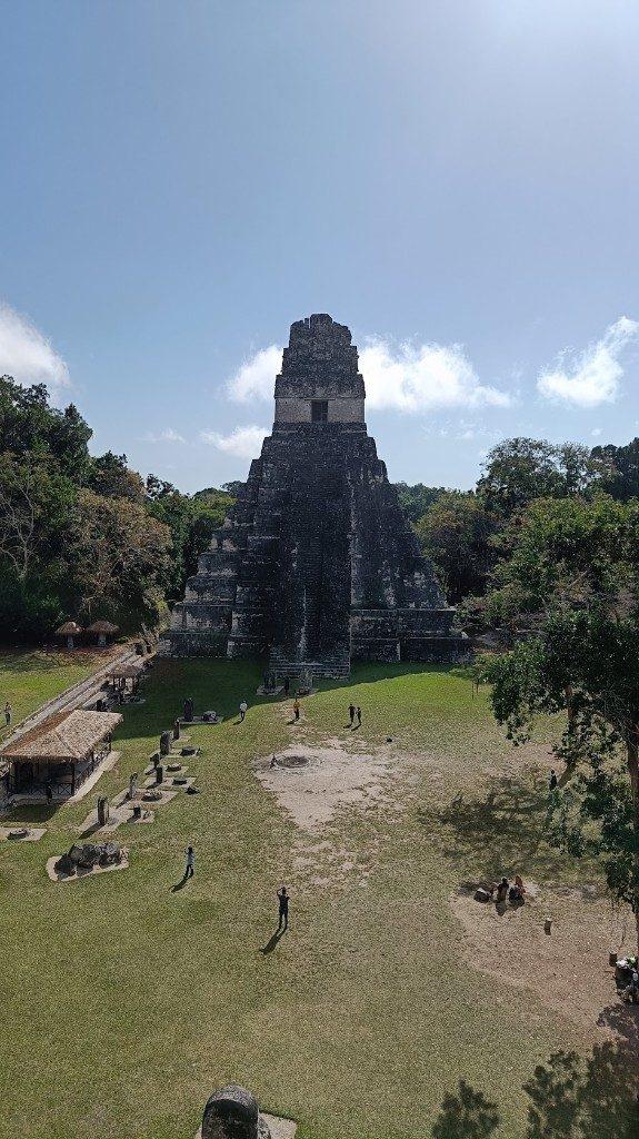 Templo maya en Tikal, con visitantes en la plaza bajo un cielo despejado.